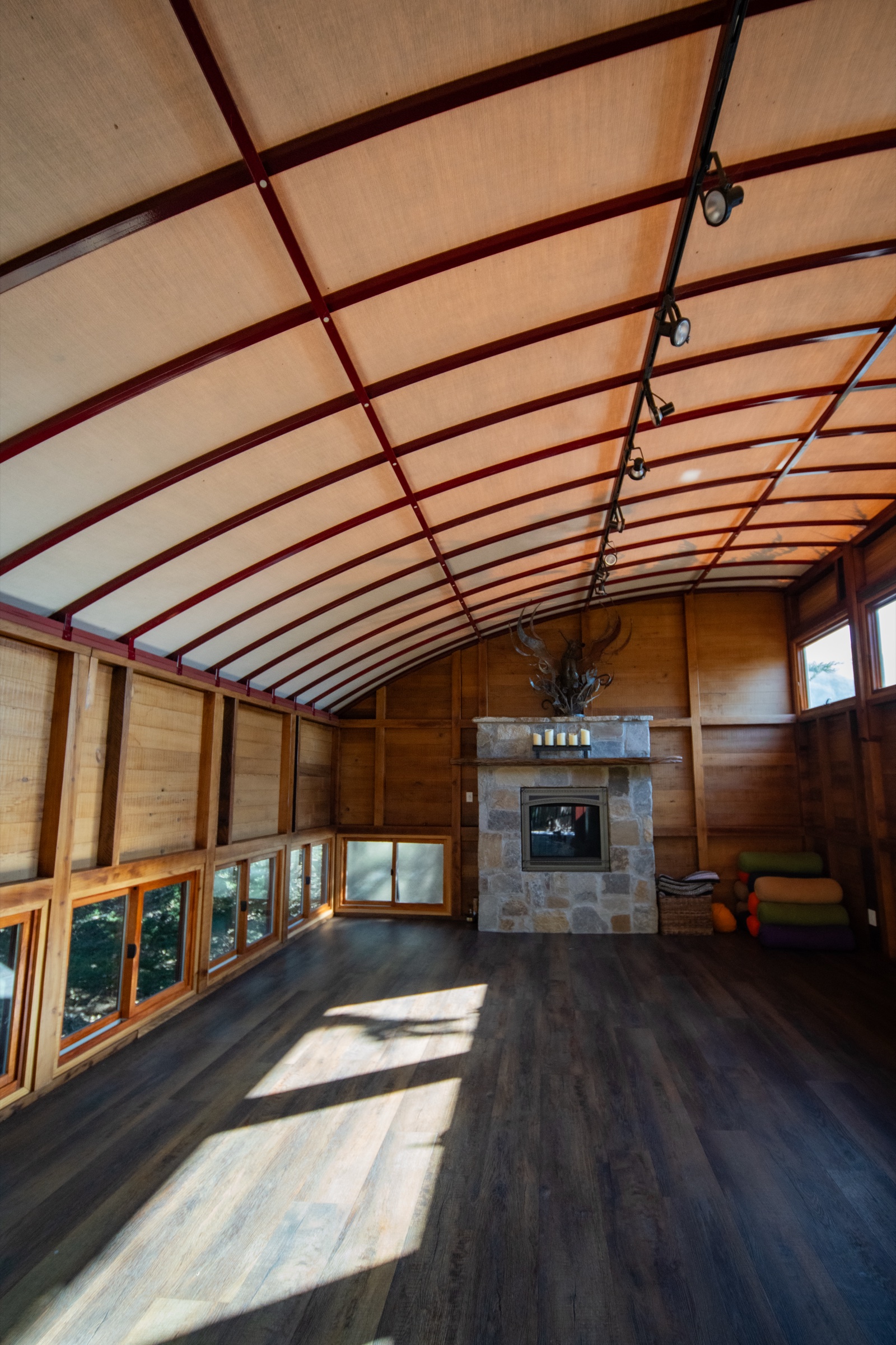 Inside the redwood yoga studio at Treebones — stone fireplace, antler chandelier, curved canvas roof, used for morning yoga when coastal weather moves practice indoors.